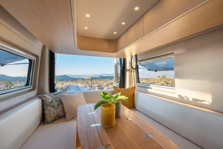 Modern RV rental interior: A cozy dining area with white benches, featuring stunning desert views through the windows.. Noovo Plus 2025