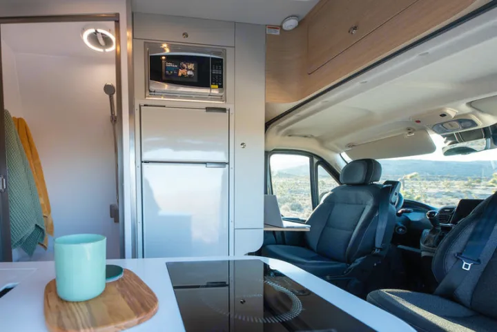 RV rental interior: kitchen (microwave, fridge, induction cooktop), compact shower, and driver's cabin with desert views.. Noovo Plus 2025