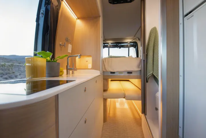 Modern rv rental interior showing a compact kitchen, sleeping area, and desert views from the window.. Noovo Plus 2025