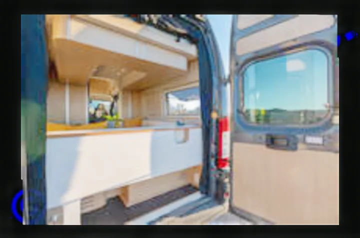 **RV rental** camper van interior from open rear doors: modern wood and white kitchenette, window view. Perfect for adventure travel.. Noovo Plus 2025