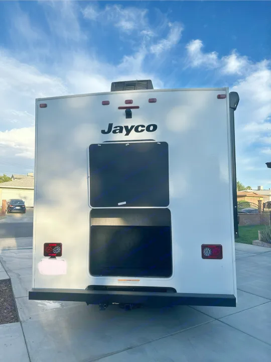 Rear view of a white Jayco RV rental under a blue sky, featuring black bunk windows and a tow hitch, ready for adventure.. JAYCO REDHAWK SE 22TF 2025