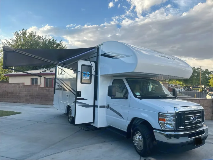 White Class C Jayco RV rental with its black awning extended, parked on a paved driveway under a cloudy sky.. JAYCO REDHAWK SE 22TF 2025