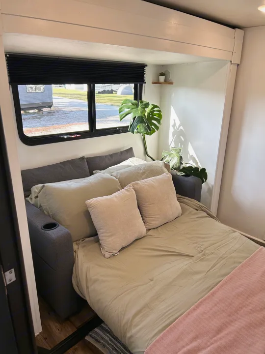 Cozy RV rental living space with a comfy pull-out bed, lush plant, and bright window views.. Highland Ridge RV Roamer 2017
