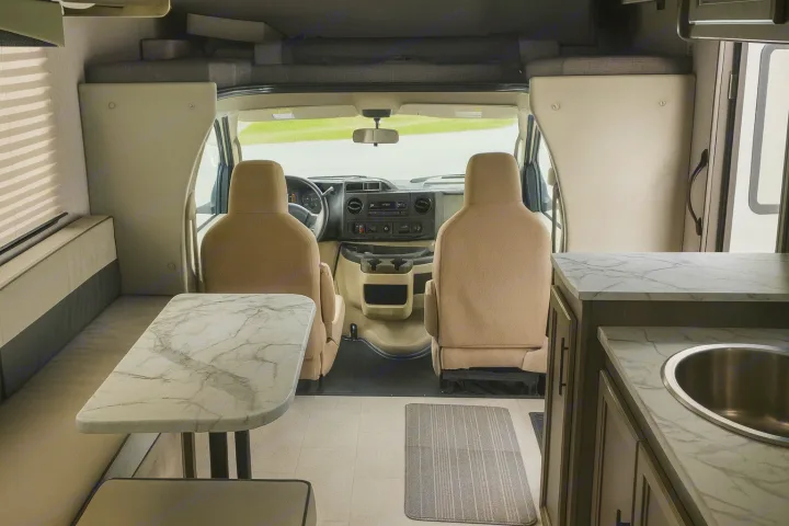 Spacious RV rental interior featuring the driver's cabin, a dining area with a marble-look table, and a kitchenette.. Coachman Freelander 22 XG 2023