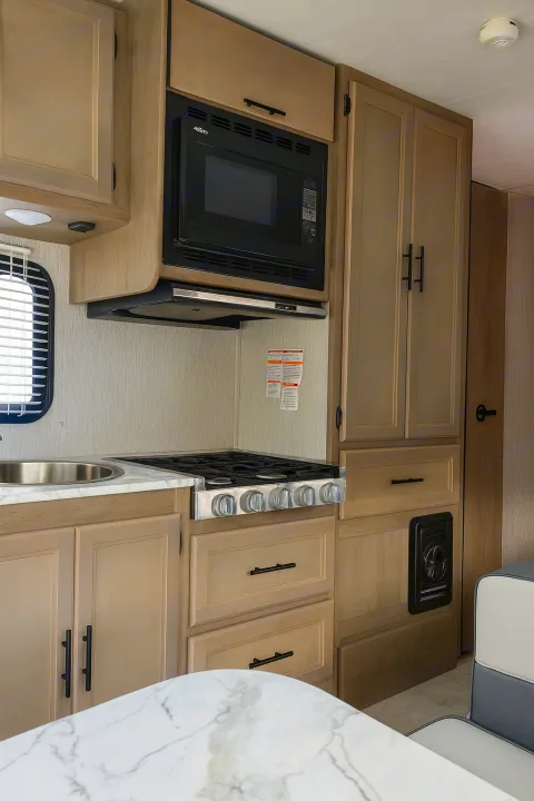 Modern RV rental kitchen with microwave, stove, sink, and light wood cabinets, perfect for a camper adventure.. Coachman Freelander 22 XG 2023