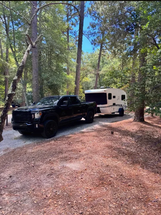 Black truck towing an RV rental parked in a sunny, wooded campsite for outdoor travel adventures.. InTech RV Sol 2023