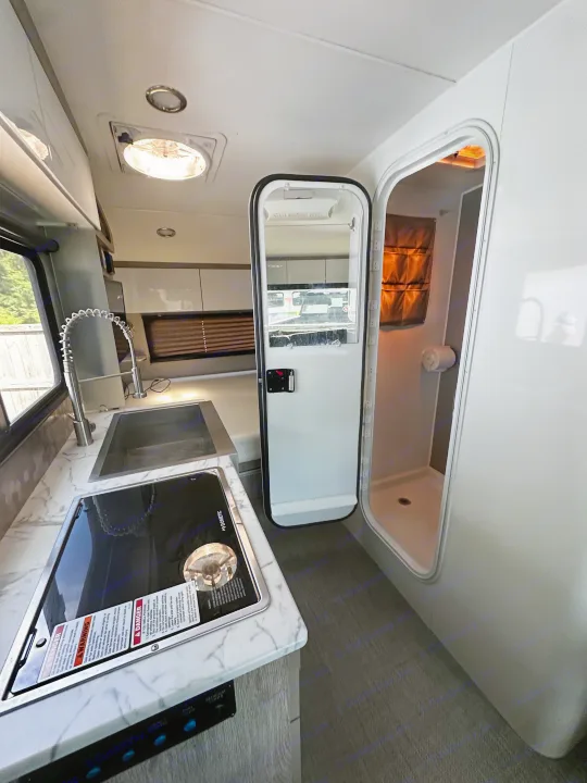 Inside an RV rental: a modern kitchen area with a sink and stove, next to a compact shower stall.. InTech RV Sol 2023