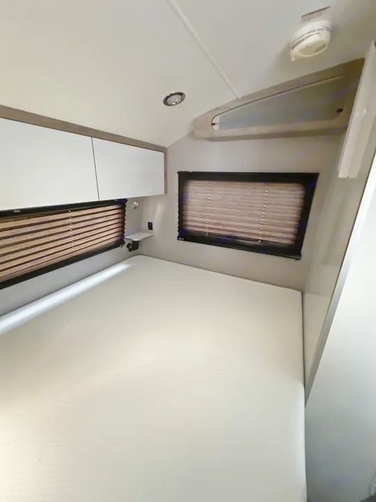 Modern RV rental sleeping area with a white mattress, sleek overhead cabinets, and dark window blinds.. InTech RV Sol 2023