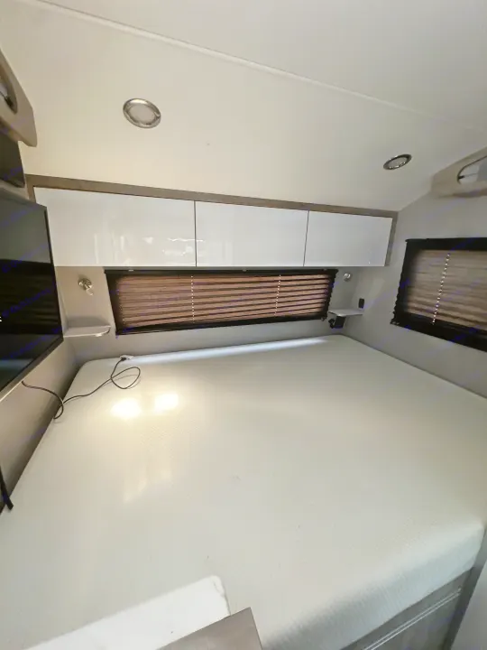 RV rental bedroom featuring a spacious mattress, bright overhead cabinets, and practical window blinds.. InTech RV Sol 2023