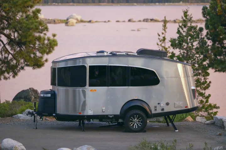 A silver Airstream Basecamp RV rental parked by a pink-hued lake at sunset, ideal for camping and outdoor adventures.. Airstream Basecamp 2022