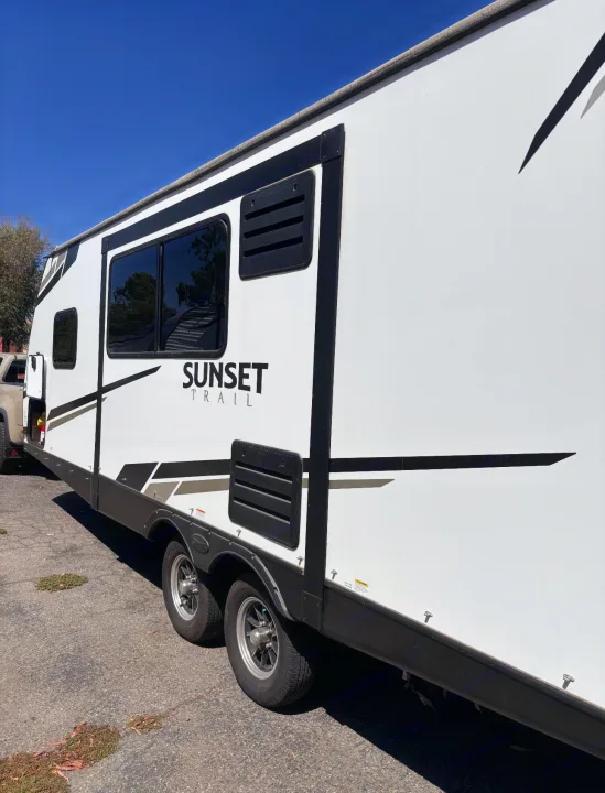 A sleek white Sunset Trail travel trailer, ideal for rv rental getaways. Features windows, vents, and tandem axles.. Crossroads RV Sunset Trail Super Lite 2022