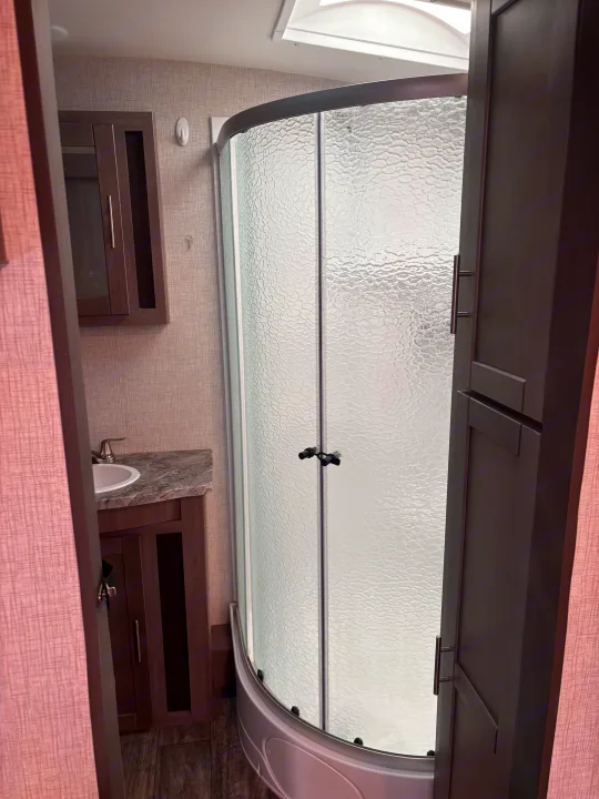 RV rental bathroom with a curved frosted glass shower, compact sink vanity, and gray-brown cabinets. Functional and modern.. Crossroads RV Sunset Trail Super Lite 2022