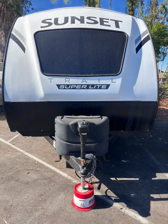 Front of a white Sunset Trail Super Lite travel trailer, an ideal RV rental, supported by a red Andersen jack block.. Crossroads RV Sunset Trail Super Lite 2022