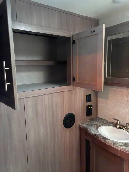 RV rental bathroom: open cabinet, sink, mirror, and wall vent, showing efficient storage and amenities.. Crossroads RV Sunset Trail Super Lite 2022