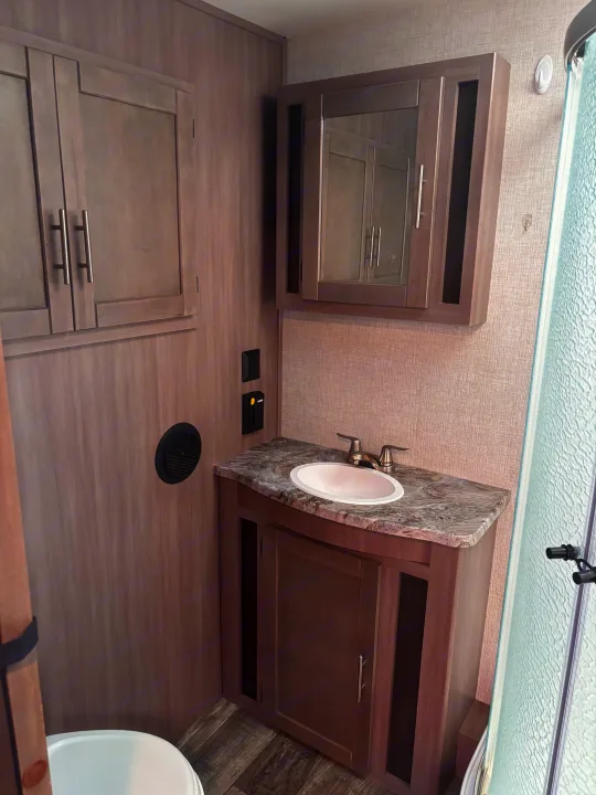Bright RV rental bathroom with wood-look cabinets, sink, mirrored medicine cabinet, and toilet. Clean, modern design.. Crossroads RV Sunset Trail Super Lite 2022