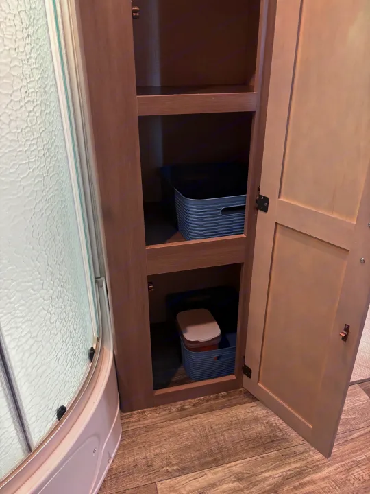 RV rental bathroom with open cabinet, showing shelves, blue storage bins, and a textured shower door.. Crossroads RV Sunset Trail Super Lite 2022