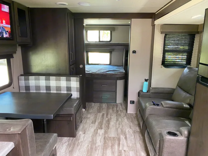 Cozy rv rental interior: dinette booth with plaid cushions, a bunk bed area, and gray reclining seats.. Grand Design Transcend Xplor 2022
