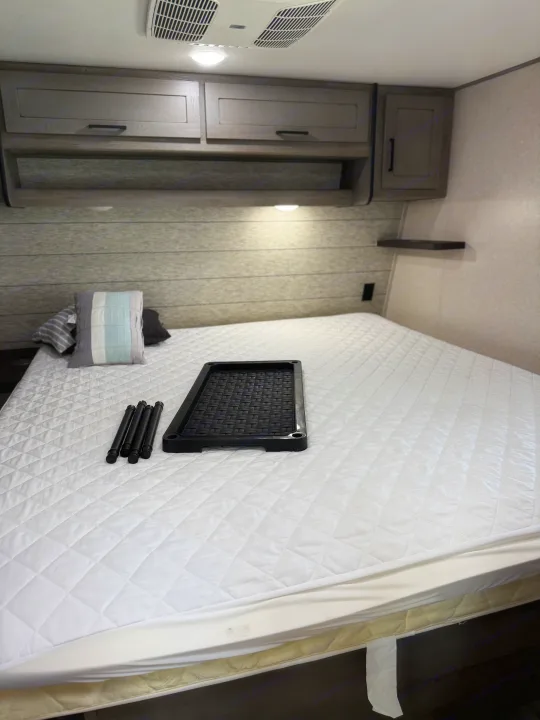 RV rental bedroom: cozy bed with quilted protector, pillows, cabinets, and a portable caddy on the mattress.. Keystone RV Raptor Toy Hauler 2021
