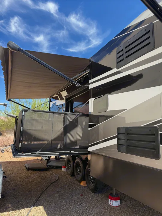 Relaxing setup of an RV rental: a large fifth wheel with an extended awning and screened patio in a sunny desert campsite.. Keystone RV Raptor Toy Hauler 2021