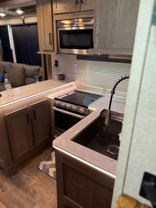 Modern RV rental kitchen: microwave, stove, sink, and illuminated countertops in a spacious interior.. Keystone RV Raptor Toy Hauler 2021