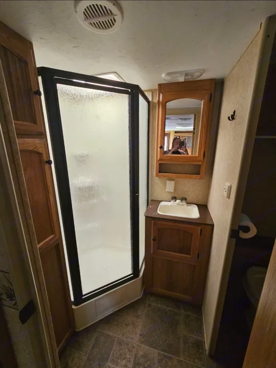 Inside an RV rental: a functional bathroom featuring a corner shower, vanity with sink, and mirror. Toilet nearby.. Dutchmen Classic 2011