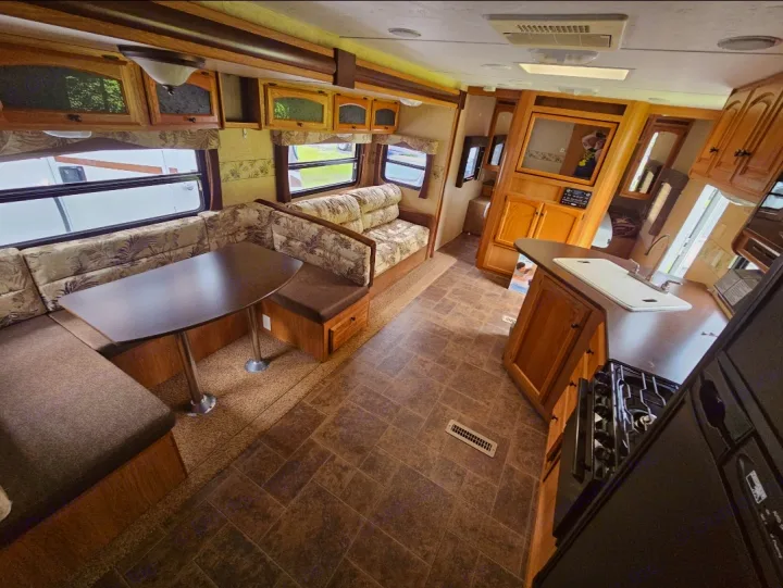 Cozy RV rental interior: dinette with table and benches, overhead cabinets, and functional kitchen area.. Dutchmen Classic 2011