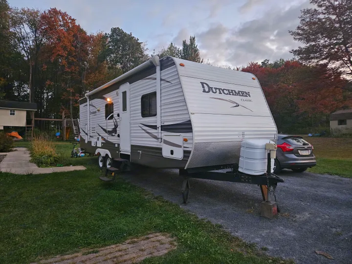 This Dutchmen Classic RV rental, with an extended awning, is parked on a gravel drive, surrounded by colorful autumn trees.. Dutchmen Classic 2011