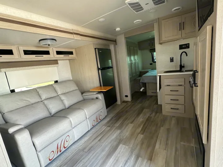 Step inside this modern RV rental interior, featuring a comfy reclining sofa, functional kitchenette, and bedroom area.. Forest River Flagstaff Micro Lite 2023