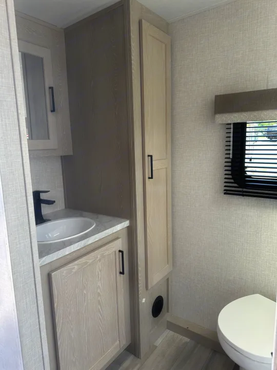 Explore this RV rental bathroom with a compact sink, toilet, ample storage, and stylish wood-grain finishes.. Forest River Flagstaff Micro Lite 2023