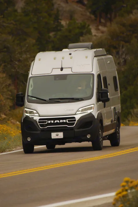 A silver Winnebago Ram ProMaster camper van RV rental drives on a scenic road with trees, ready for adventure.. Winnebago Soilis 2025