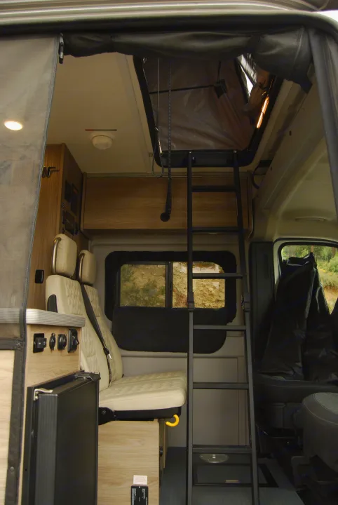 RV rental interior showing a ladder to a pop-top bed, plush seating, and controls for a comfortable camper experience.. Winnebago Soilis 2025