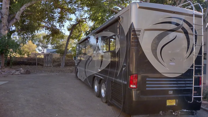 Luxury RV rental parked under trees in a natural setting. This large motorhome features unique graphics and a rear ladder.. Country Coach Allure 470 2005
