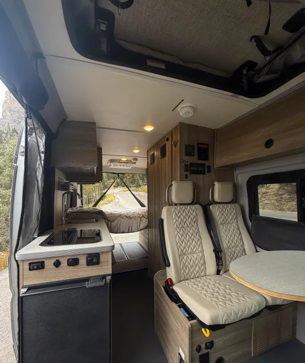 Cozy rv rental camper van interior featuring a compact kitchen, comfortable seating, and a rear bed with mountain views.. Winnebago Soilis 2025