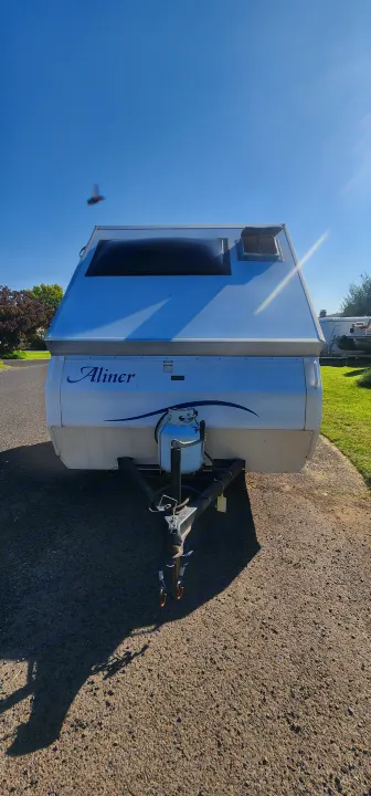 Front view of a white A-liner pop-up camper, showing its propane tank and hitch. Ready for an RV rental adventure on a bright, sunny day.. A Liner A Liner Popup Trailer 2006