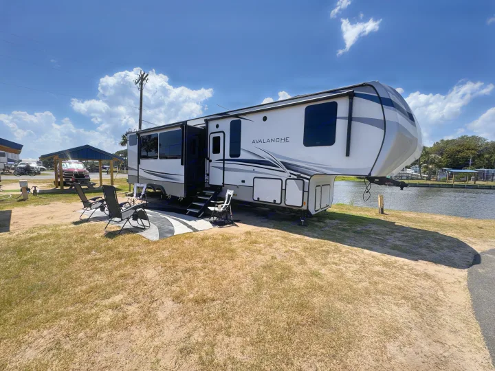 This Avalanche fifth-wheel RV rental is perfectly set up for a relaxing vacation by the water at a sunny campground.. Keystone RV Avalanche 2022