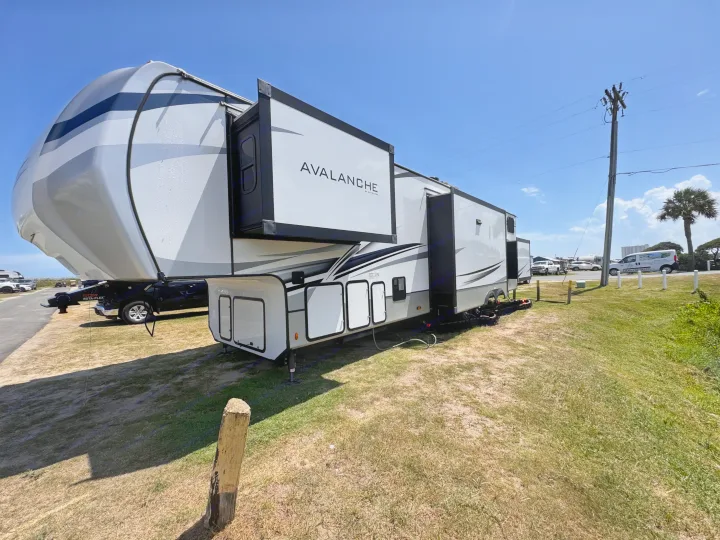 This Avalanche fifth-wheel rv rental, featuring extended slide-outs, is parked at a sunny campsite, ready for adventure.. Keystone RV Avalanche 2022