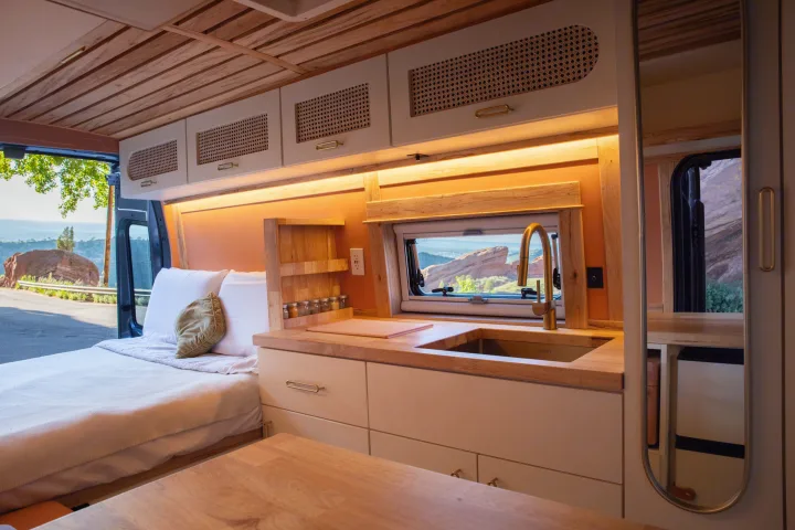 Cozy rv rental interior with a fully equipped kitchen, comfortable bed, and a stunning scenic view out the window.. Ford Transit 2023