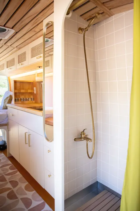 Stylish RV rental interior with compact shower, brass fixtures, and kitchenette. Perfect for cozy van life adventures!. Ford Transit 2023