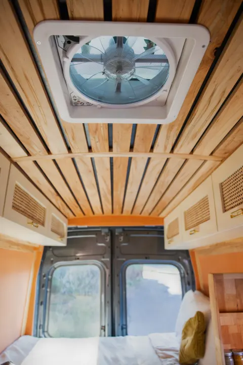 Looking up inside an RV rental: wood-slat ceiling, rooftop vent, overhead cabinets, and bed in a cozy camper van.. Ford Transit 2023