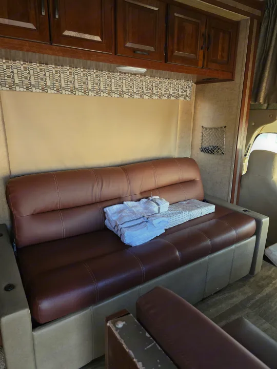 Spacious RV rental interior with a comfy brown sofa, overhead cabinets, decorative valance, and practical mesh storage.. Forest River Sunseeker 2016