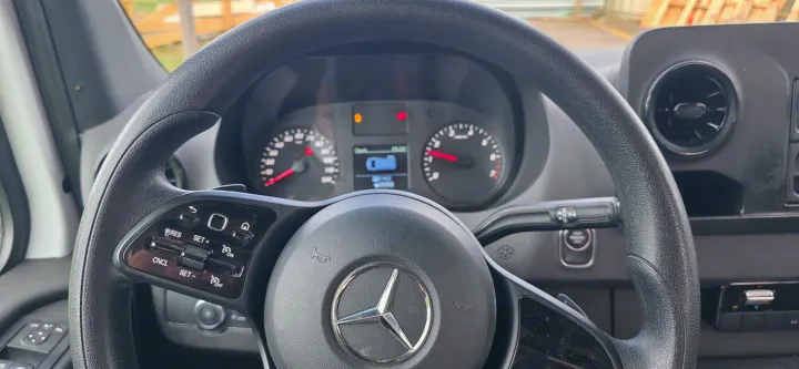 Inside a Mercedes-Benz RV rental: steering wheel, dashboard, controls, and illuminated gauges.. Mercedes-Benz Sprinter 2024
