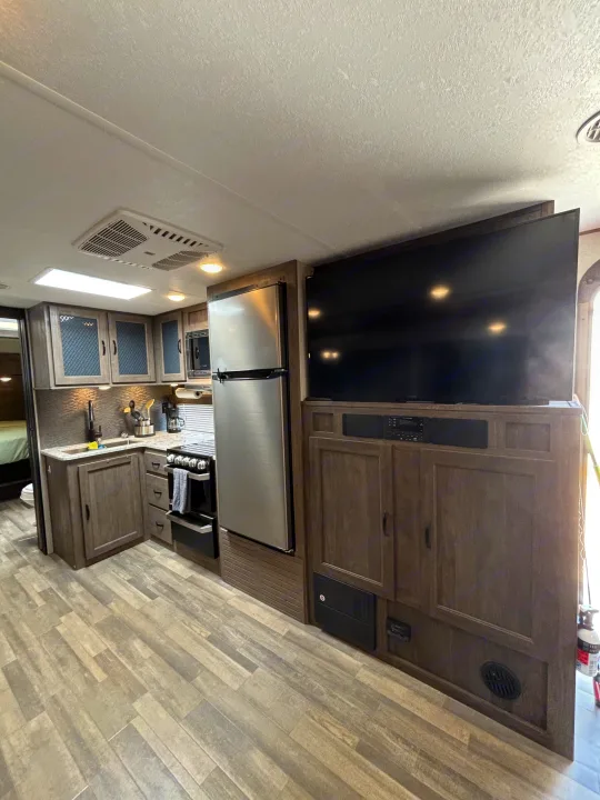 Inside this RV rental: A modern kitchen with full-size fridge, stove, and a large TV for comfortable journeys.. Forest River Vibe 2021