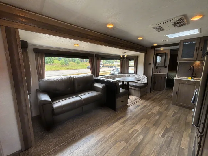 Modern rv rental's living space with a dark sofa, U-shaped dinette with checkered accents, wood-look floor, kitchen, and bath access.. Forest River Vibe 2021