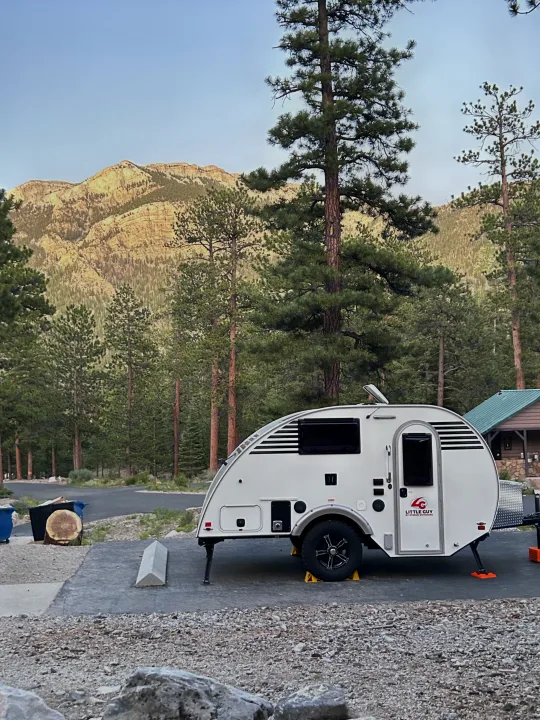 A white Little Guy rv rental teardrop trailer at a scenic mountain campsite, surrounded by towering pine trees.. Xtreme Outdoors Xtreme Outdoors Trailer 2022