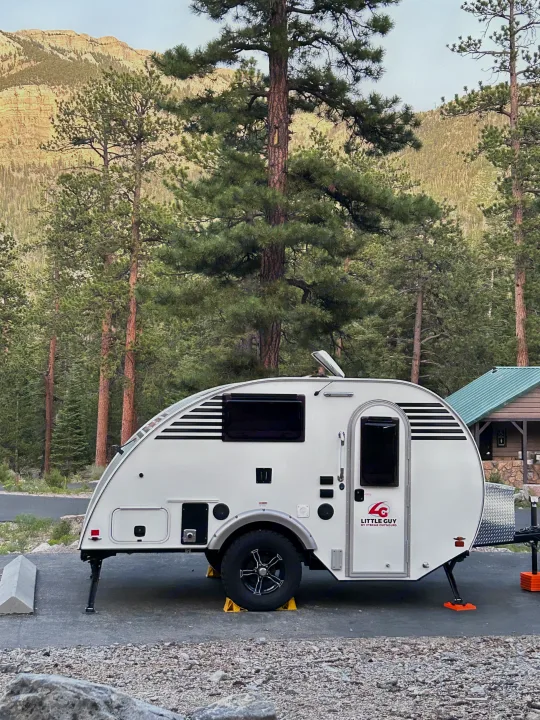 White Little Guy teardrop travel trailer, ideal for an RV rental, parked amidst tall pine trees at a mountain campsite.. Xtreme Outdoors Xtreme Outdoors Trailer 2022
