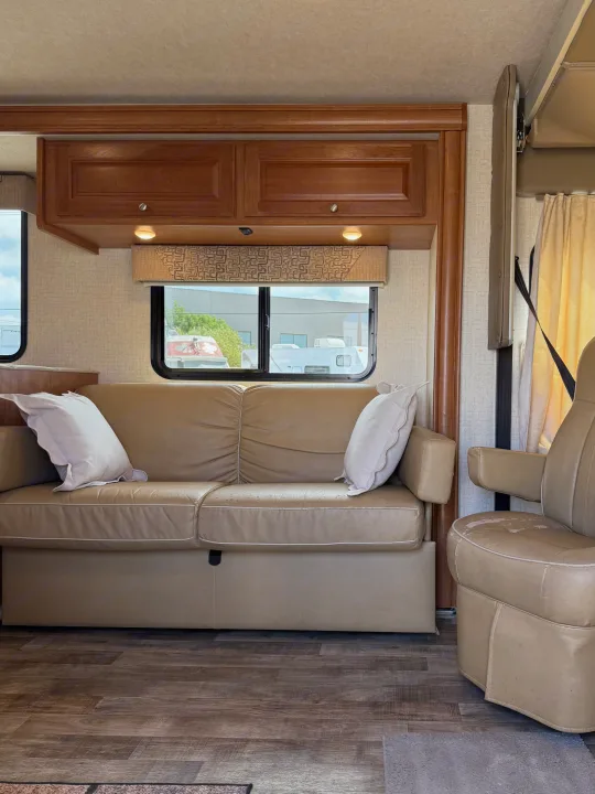RV rental living space with a tan sofa, individual seat, wooden cabinets, windows, and hardwood-style flooring.. Winnebago Vista 2017