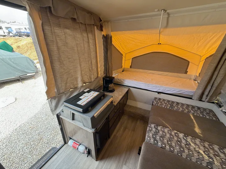 Experience this cozy RV rental interior, featuring a bed, kitchen counter with coffee maker/stove, seating, and outdoor view.. Forest River Flagstaff M.A.C. 2022