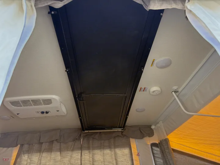 Overhead inside an RV rental, showing the camper ceiling with an AC unit, dome lights, smoke alarm, and a central black pop-up panel.. Forest River Flagstaff M.A.C. 2022