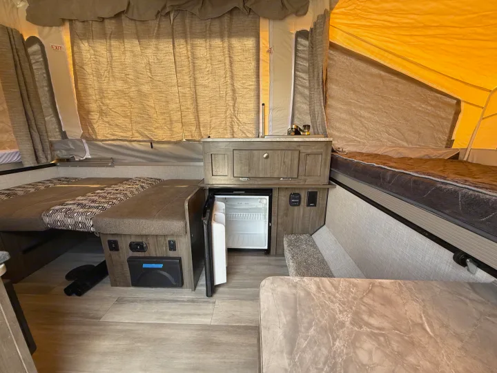 This rv rental interior features sleeping areas, a mini-fridge, a sink, and dining space, ideal for camping or travel.. Forest River Flagstaff M.A.C. 2022