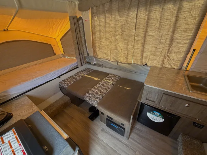 Inside an RV rental pop-up camper: a cozy dinette with patterned cushions, a bed, and a compact kitchen with a sink and mini-fridge.. Forest River Flagstaff M.A.C. 2022